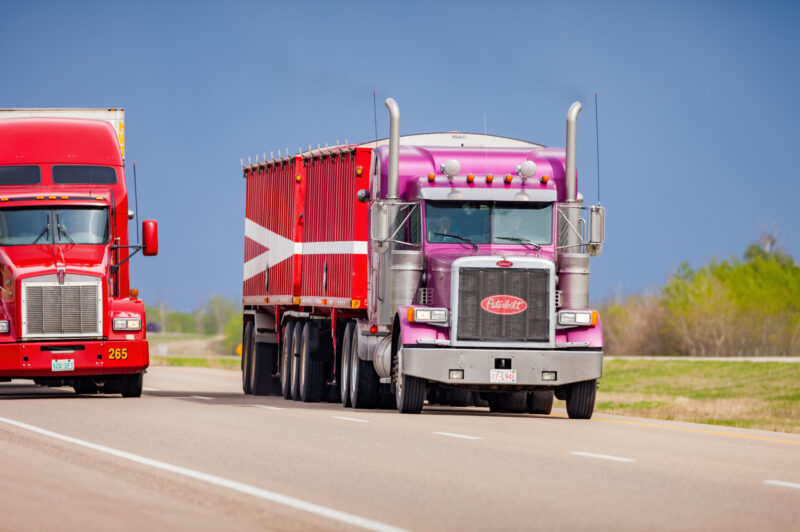 Two semi trucks drive on Highway 16 (Yellowhead Highway) between Lloydminster and Battleford, Saskatchewan, Canada on a cloudy day.