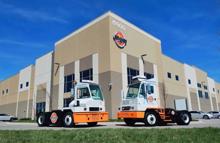 Two orange EV trucks in front on the facility